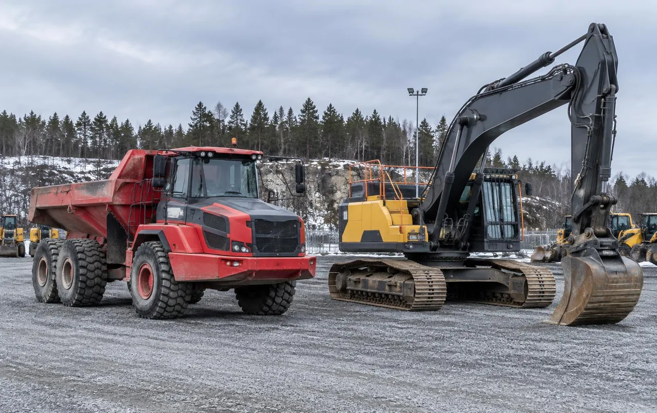 Gul dumper framför en bandgrävmaskin på en grusad auktionsplats